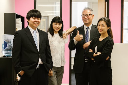 Group of Asian professionals in corporate attire smiling and posing in a modern office setting.