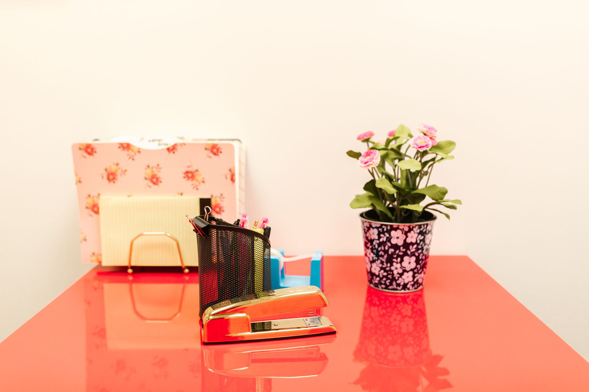 A colorful office desk arrangement featuring a red stapler and potted flowers.