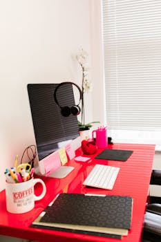 Bright red desk setup featuring an iMac, headphones, and a coffee-themed mug, ideal for a creative workspace.