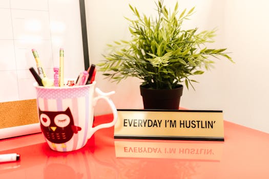 Bright desk setup featuring a motivational quote, potted plant, and cup of pens.