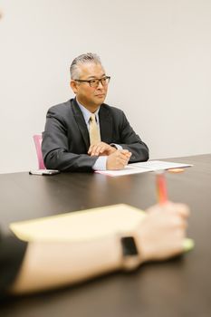 Senior executive in a formal business meeting, wearing a suit and eyeglasses, indoors.