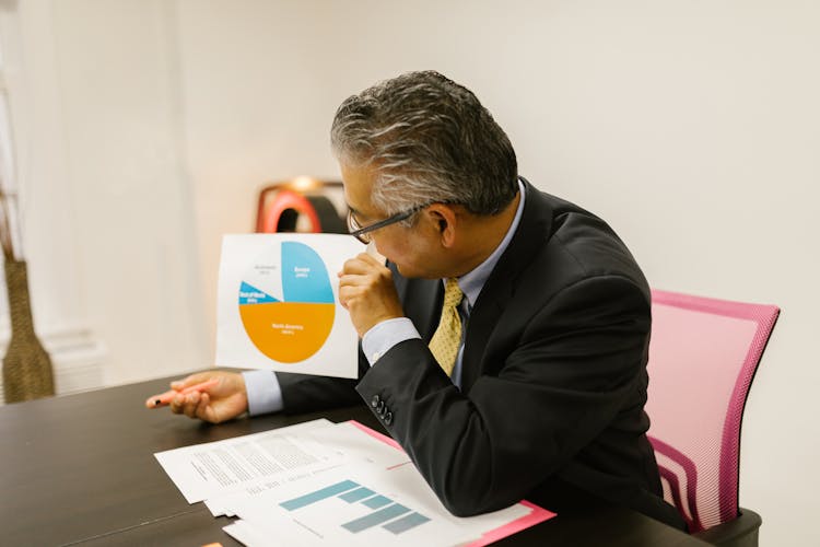 A Businessman Holding A Paper With Printed Graph