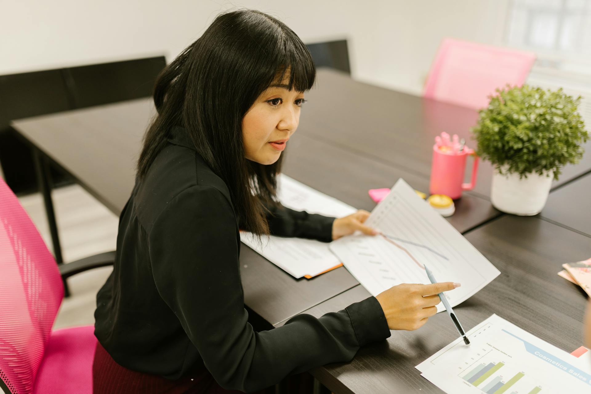 Young Asian businesswoman reviewing charts in a modern office. Professional and focused setting.