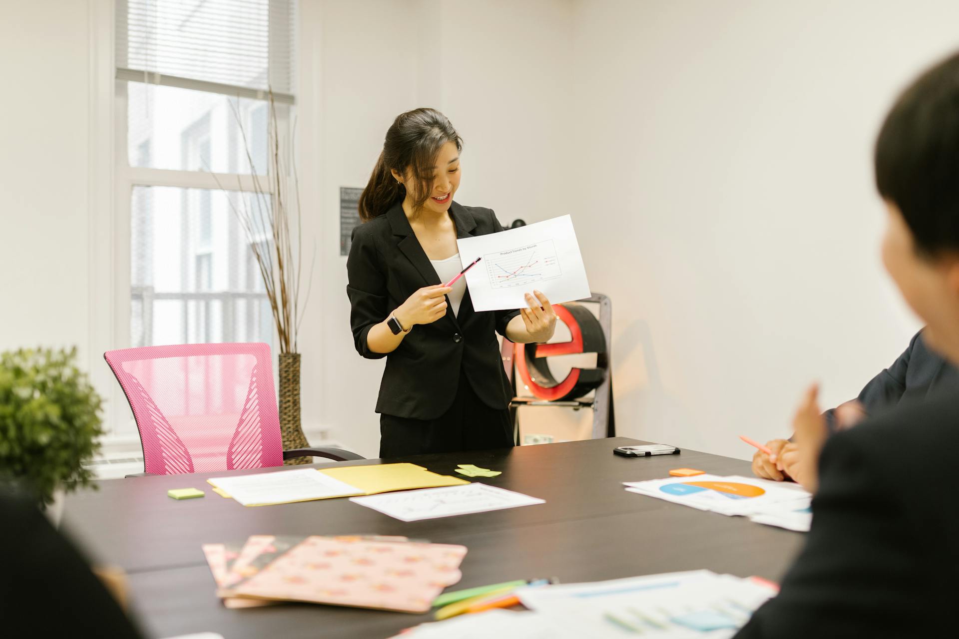 Asian business team in a meeting, presenting charts and discussing strategies in a modern workspace.