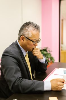 Mature businessman in a suit reviewing financial documents at desk.