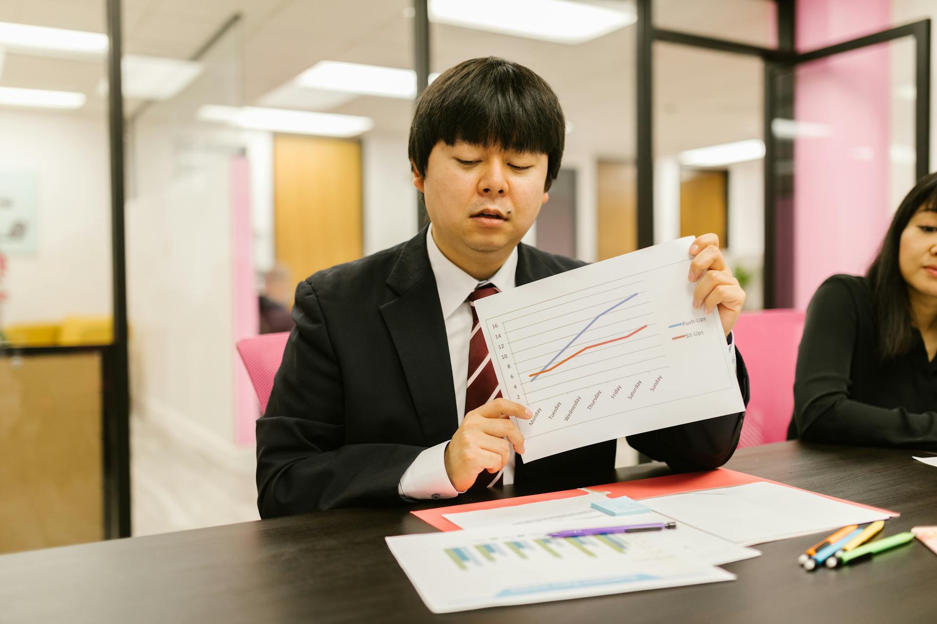 Two professionals in business attire discussing graphs during an office meeting.