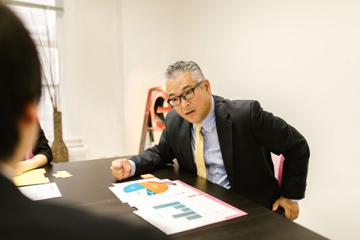 A focused businessman in a meeting, analyzing and discussing printed graphs.