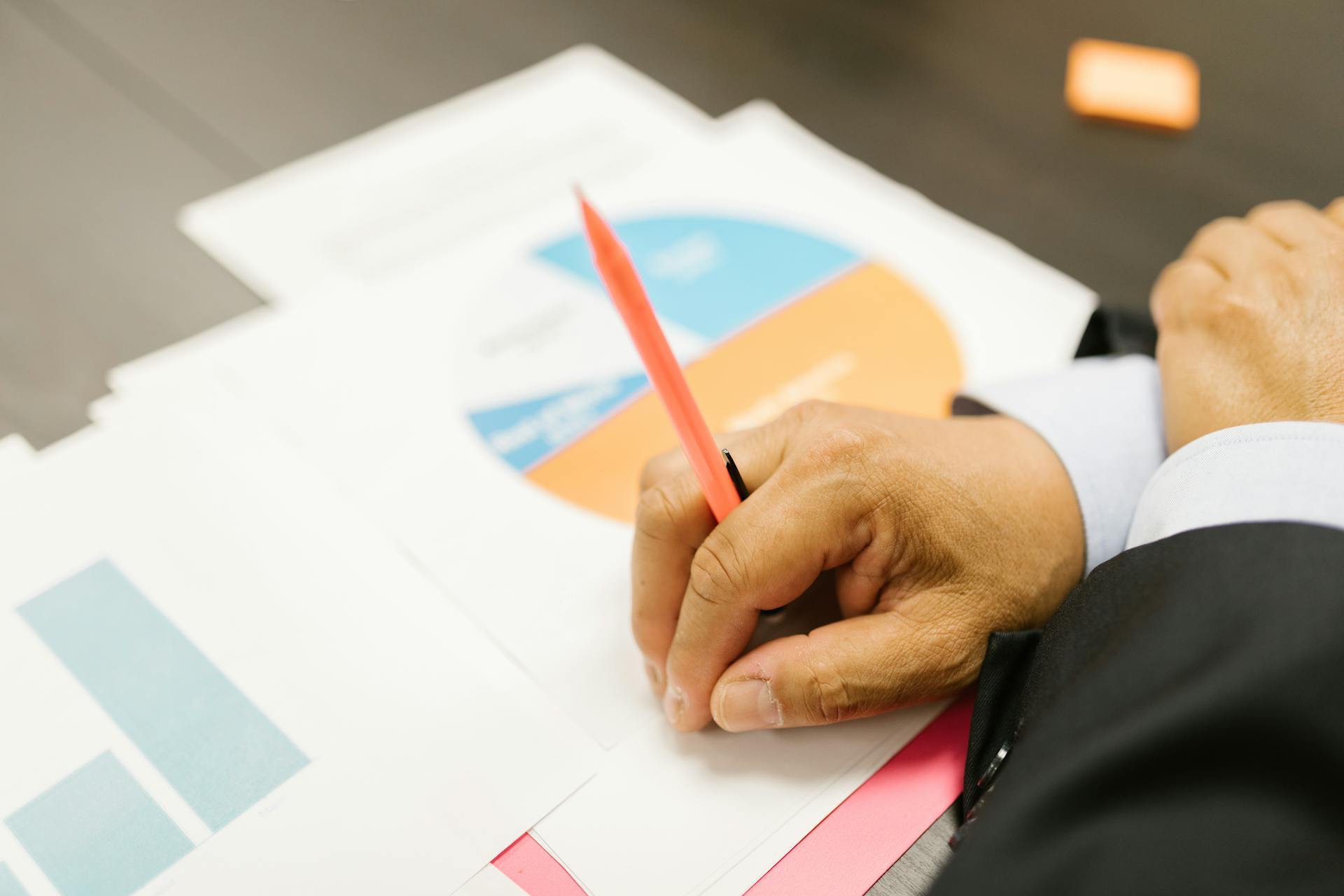 A businessman writing on financial documents with charts in an office setting.