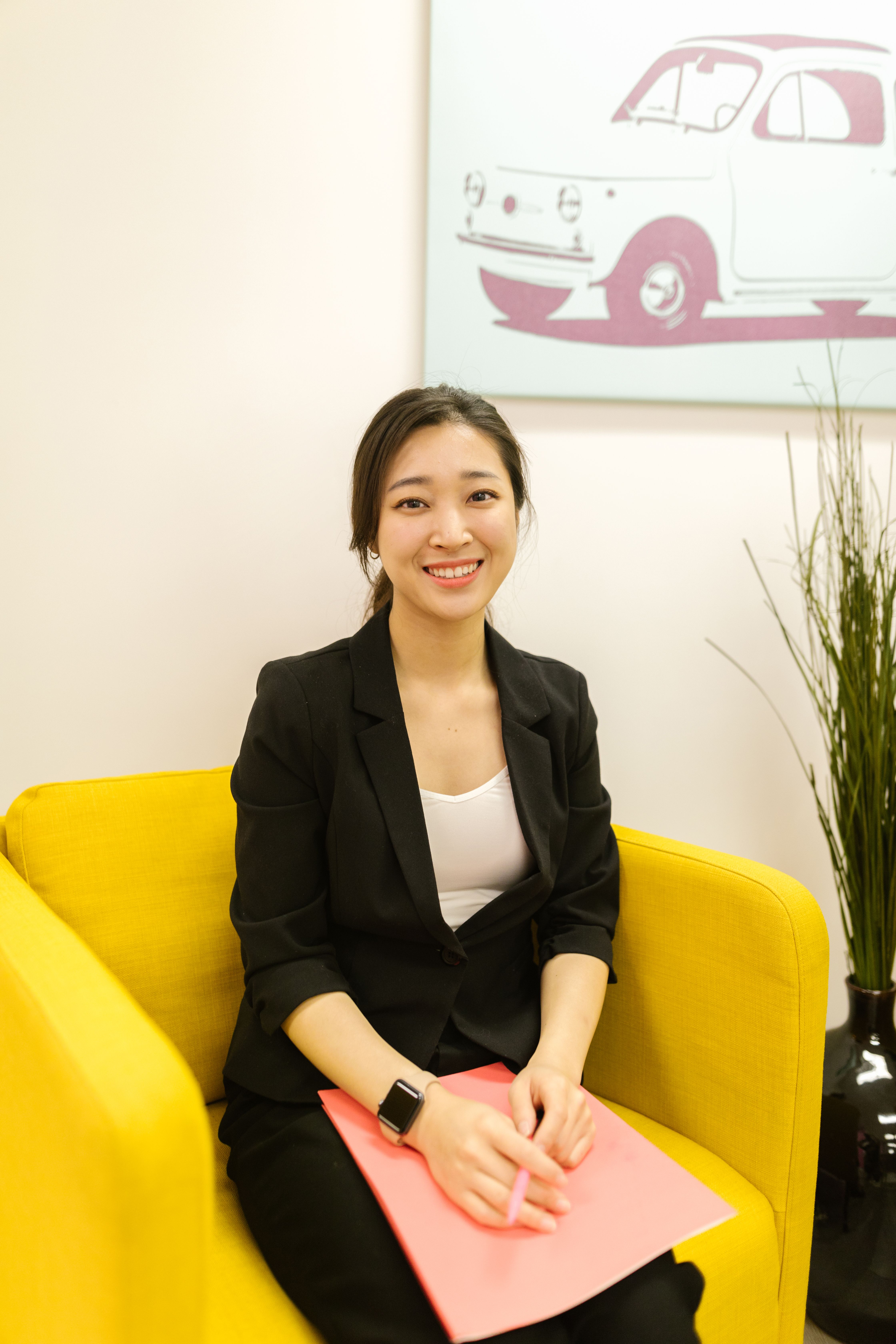 Smiling businesswoman sits on a vibrant yellow sofa with a modern interior backdrop.
