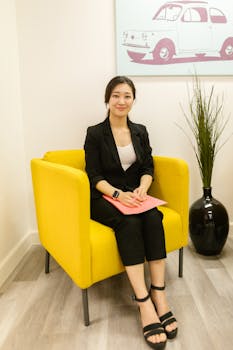 Asian businesswoman in corporate attire sits confidently in a modern office setting.