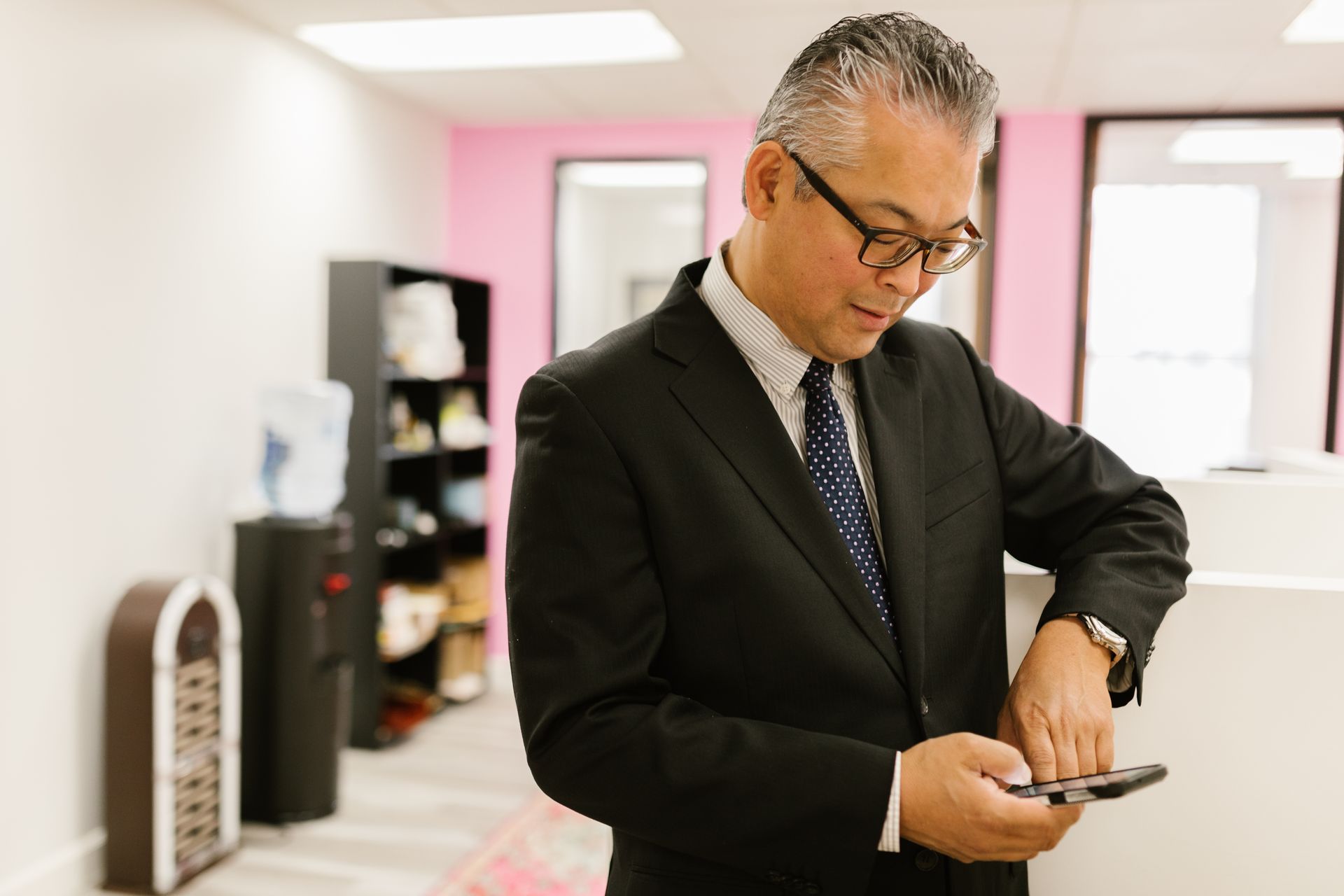 A professional man in a business suit texting on his smartphone in a modern office setting.