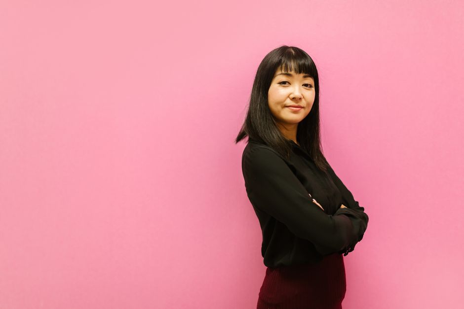 ピンクの背景の前に立ち、腕を組んだ自信に満ちた女性。