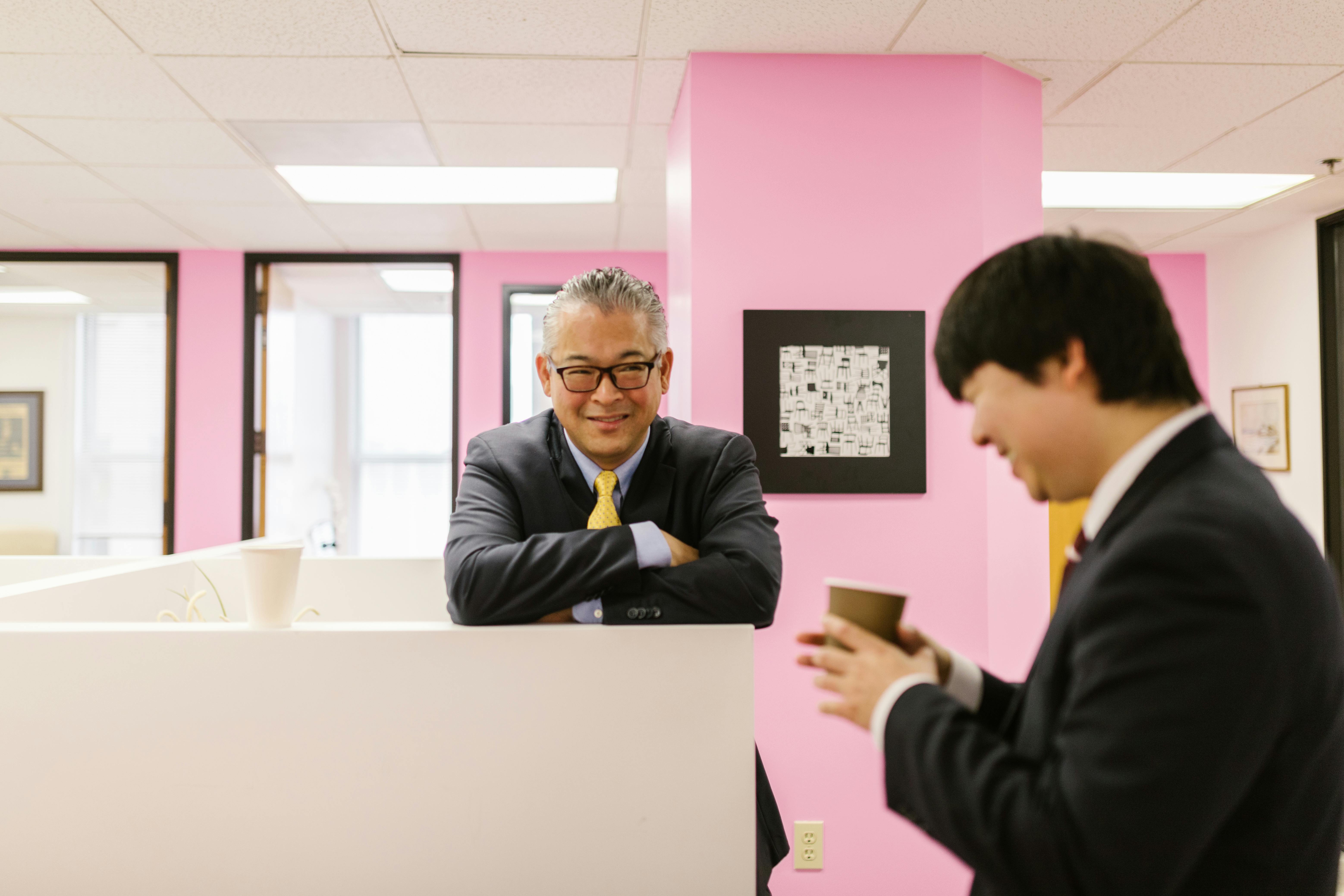 Man in Black Suit Leaning with Arms on White Panel