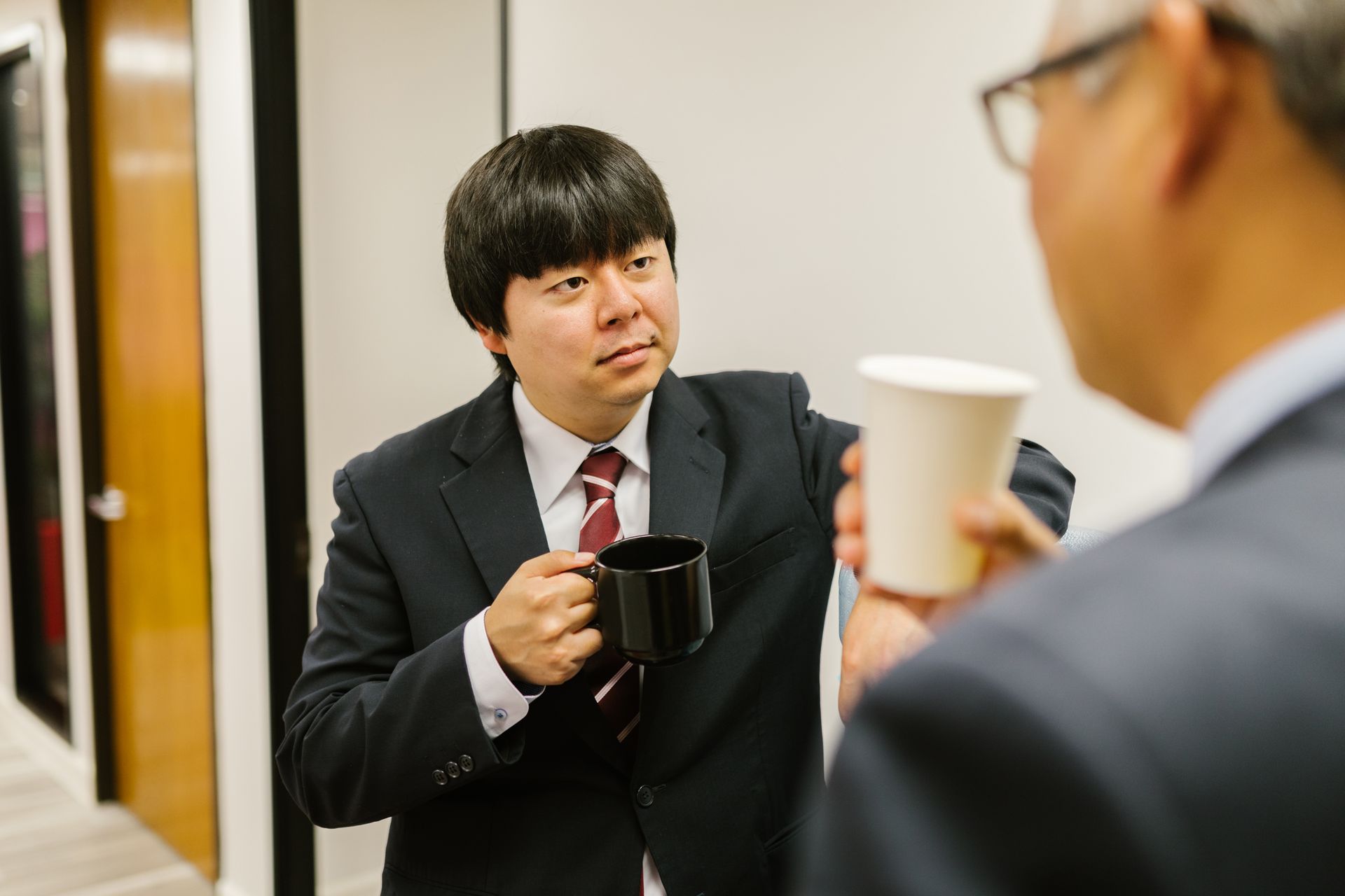 Two business professionals enjoying a coffee break and conversation inside an office setting.