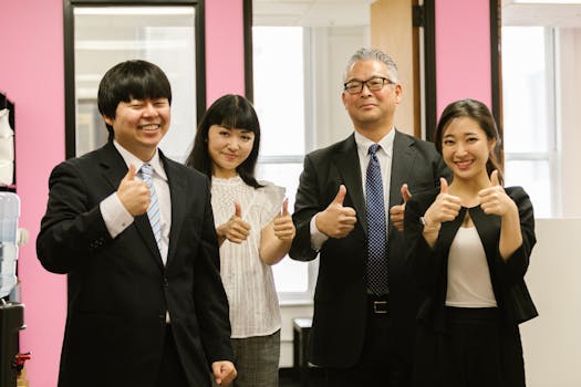 A joyful group of business professionals giving thumbs up in an office setting, signifying achievement and teamwork.