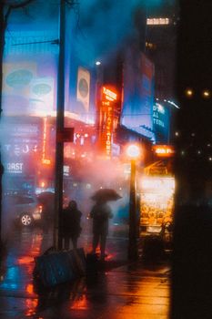 People walking on street between high rise buildings in modern city in rainy day in night time