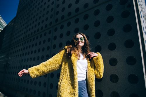 Free Stylish woman wearing a yellow fur coat poses confidently outdoors in daylight. Stock Photo
