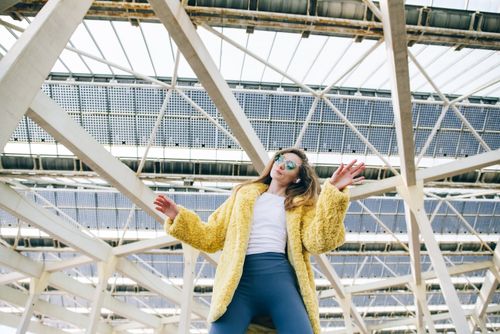 Free Fashionable woman in yellow faux fur coat and sunglasses under modern architecture. Stock Photo