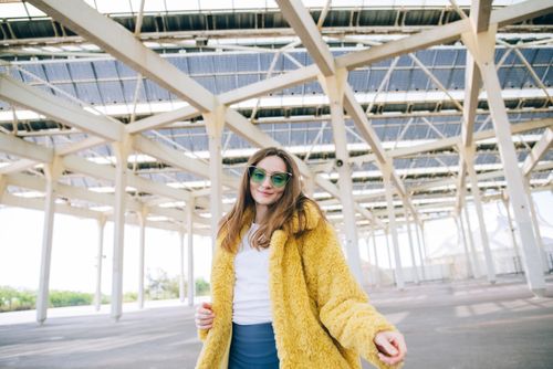 Free Stylish woman in a yellow faux fur coat posing confidently outdoors. Stock Photo