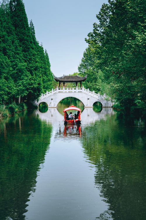 Free Oriental pleasure boat with tourists floating on peaceful water of lake near footbridge in greenery terrain Stock Photo