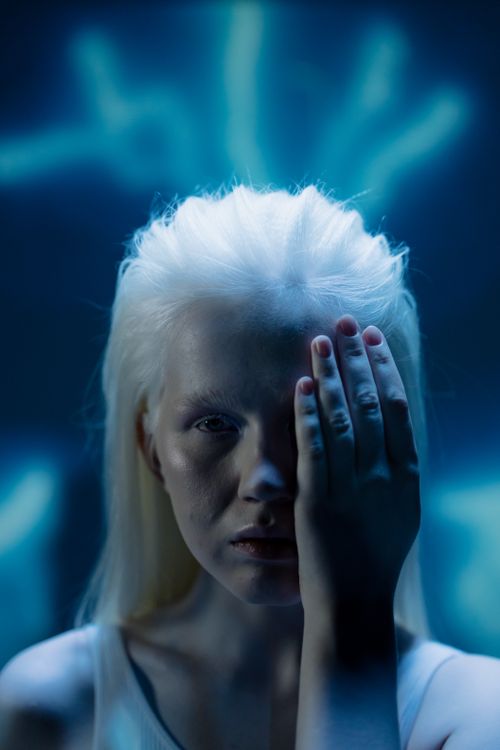 Free Close-up portrait of an albino woman posing with hand covering her face in a conceptual art setting. Stock Photo