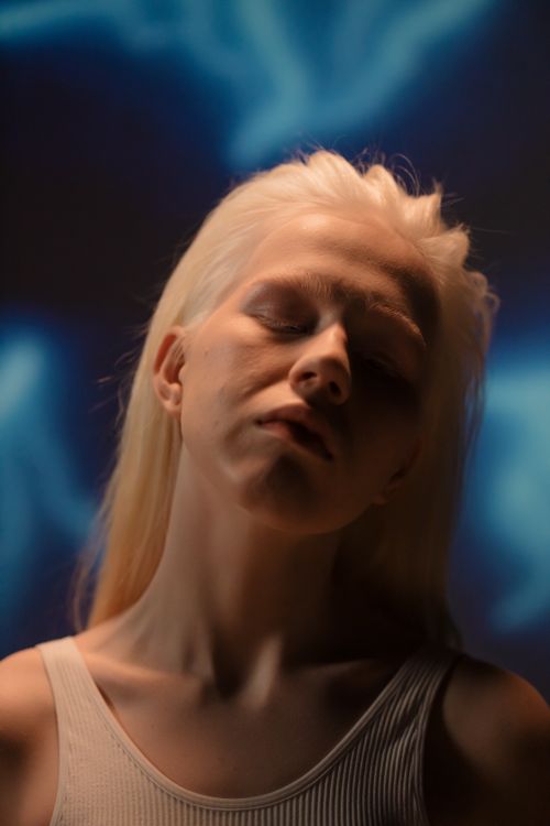 Free Artistic portrait of a woman with blonde hair and eyes closed, wearing a tank top. Stock Photo