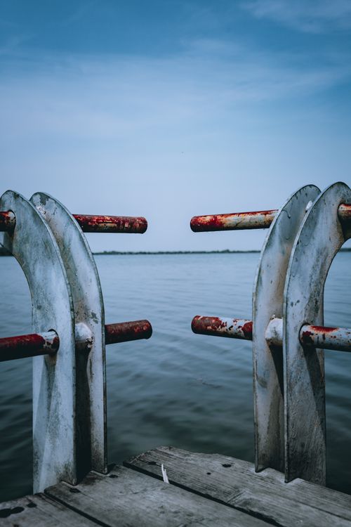 Free Wooden pier with shabby metal railing of fence over calm water of river on sunny day Stock Photo
