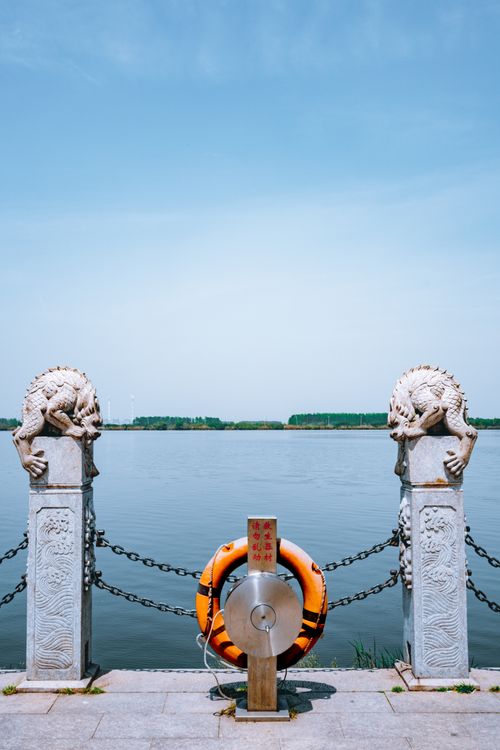 Free Picturesque view of calm water of blue sea and stone fence with sculptures and orange lifebuoy Stock Photo