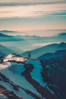 A lone hiker stands triumphantly on a snow-covered peak with a breathtaking view of the Himalayas during sunrise.