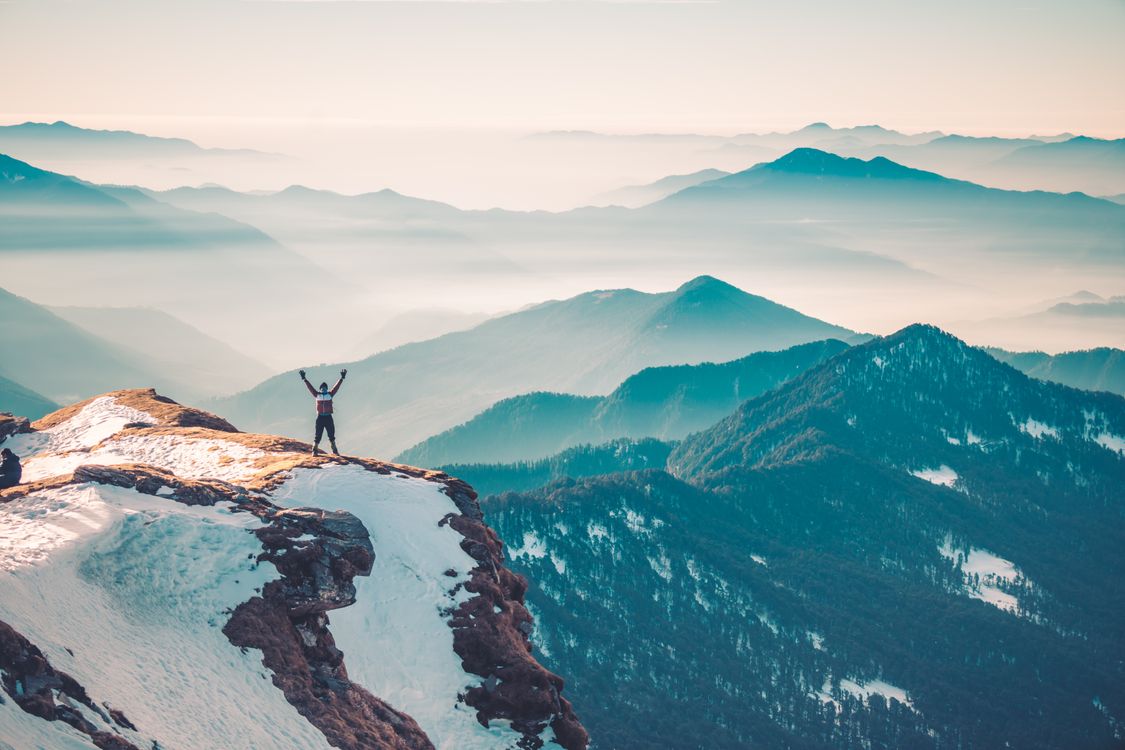 Person standing on mountain peak above the clouds with arms raised - freedom architect