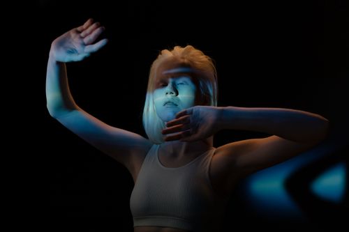 Free Artistic portrait of a woman with hands raised, illuminated by blue light and shadows. Stock Photo