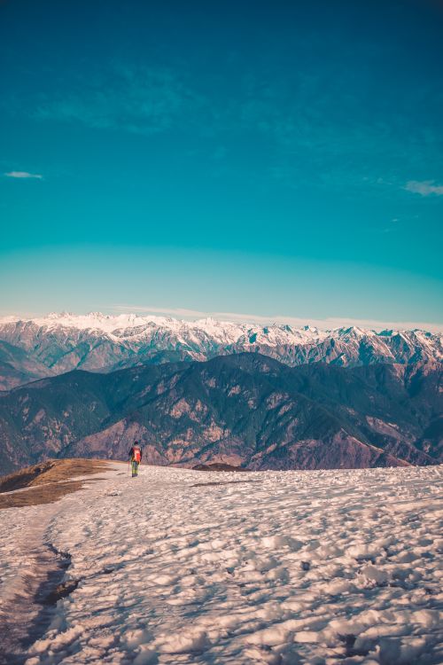 Free A lone figure stands on a snowy mountain slope with a stunning view of distant peaks. Stock Photo