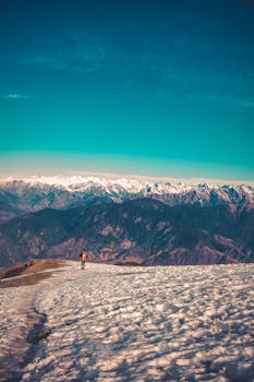 A lone hiker treks through snow-covered mountains under a clear blue sky, embracing adventure.