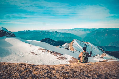 A Person Holding a Stick Sitting on a Snow Covered Mountain