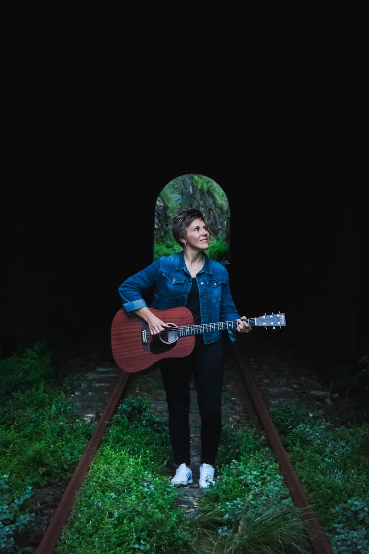 Woman Standing On Railroad Track Playing Guitar