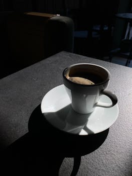 Dark espresso cup casting shadows on table in sunlit café for a moody vibe.