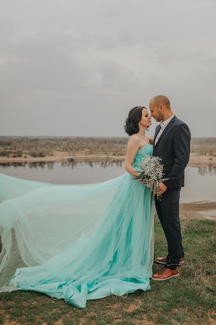 Newlywed Couple Embracing On River Shore On Wedding Day