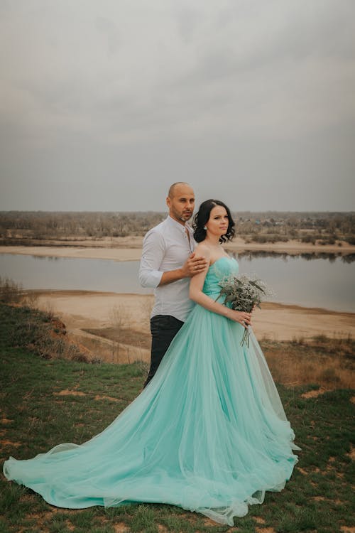 Newlywed couple contemplating river from shore in countryside