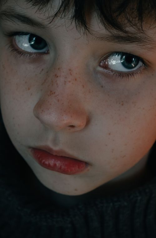 Free Intense portrait of a child with freckles, showcasing vivid green eyes and red lips. Stock Photo