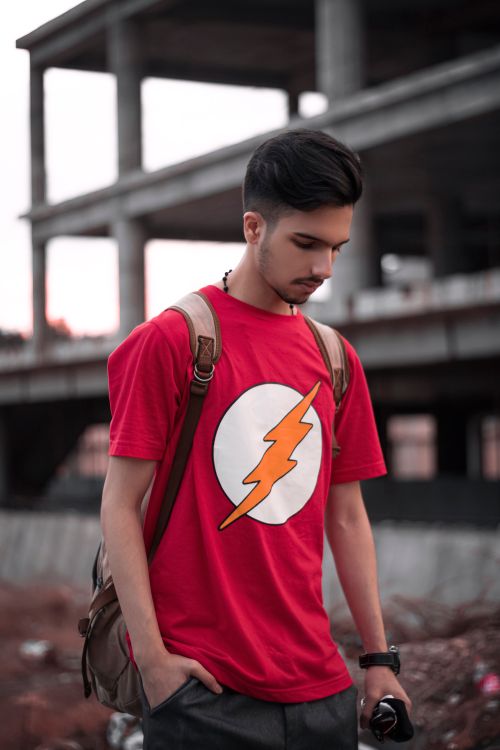Free A young man in a red t-shirt with a lightning bolt symbol stands in an urban setting. Stock Photo