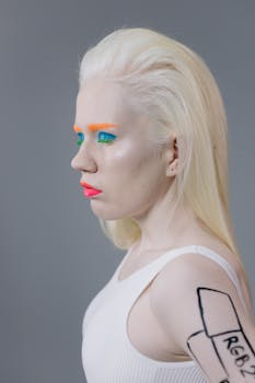 Profile shot of an albino woman with vibrant makeup against a gray background in a studio.