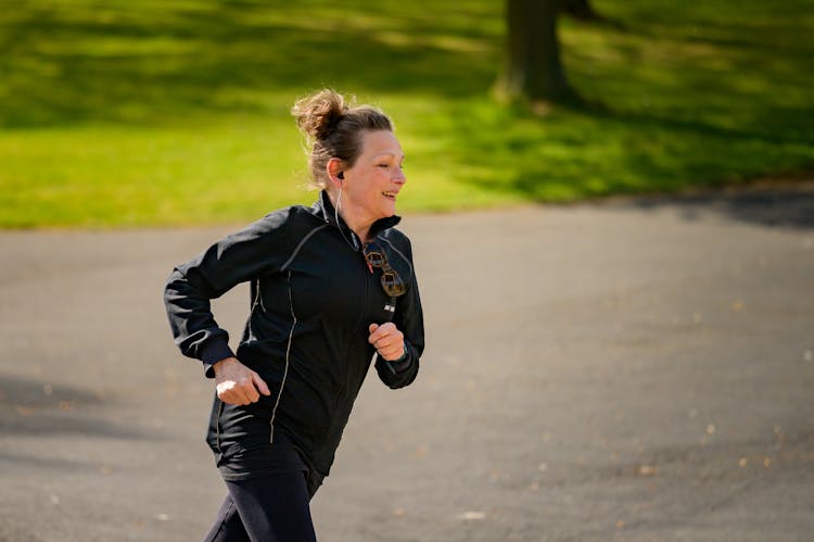 Woman In Active Wear Jogging On Gray Asphalt Road