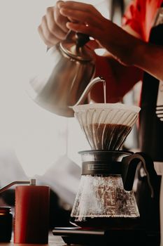 Close-up of a barista manually brewing pour over coffee in a cafe setting.