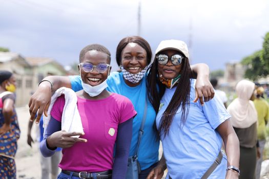 Three friends smiling and posing together while volunteering outdoors on a sunny day.