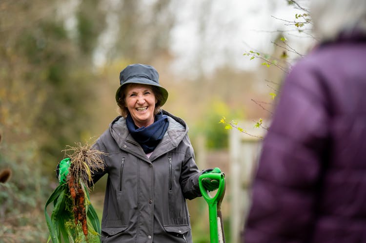 Woman In Black Jacket Holding Shovels And Plant 