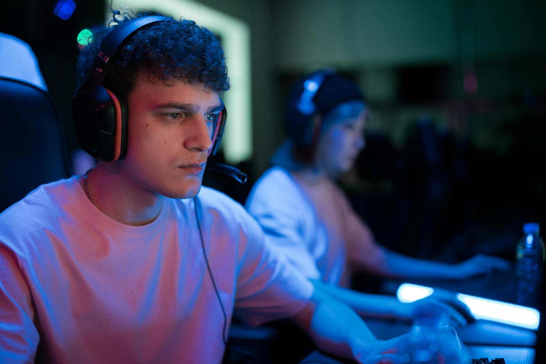 Man with headset engaged in intense gaming session under neon lights.