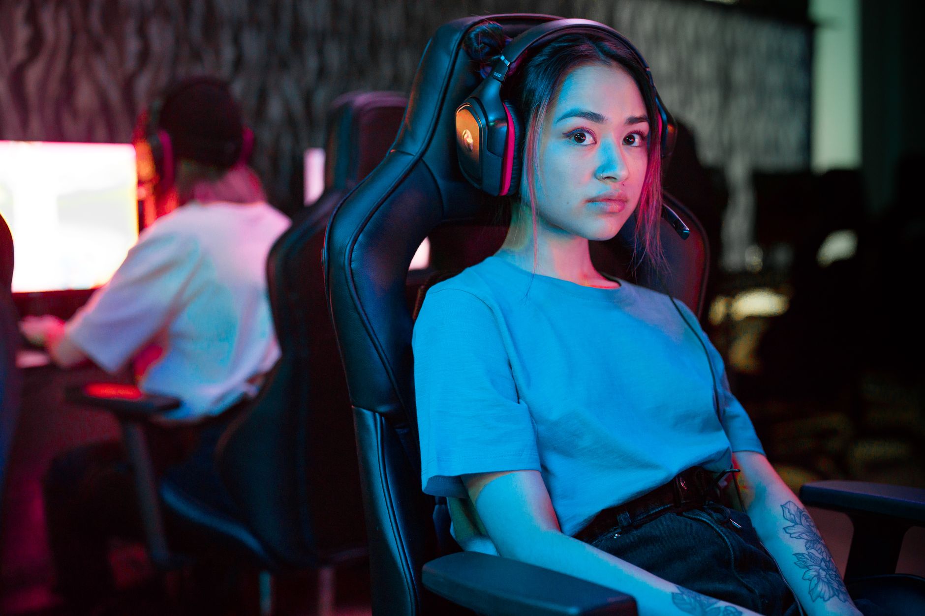 Jeune femme avec casque audio assise dans un fauteuil gaming, éclairage néon bleu et rose