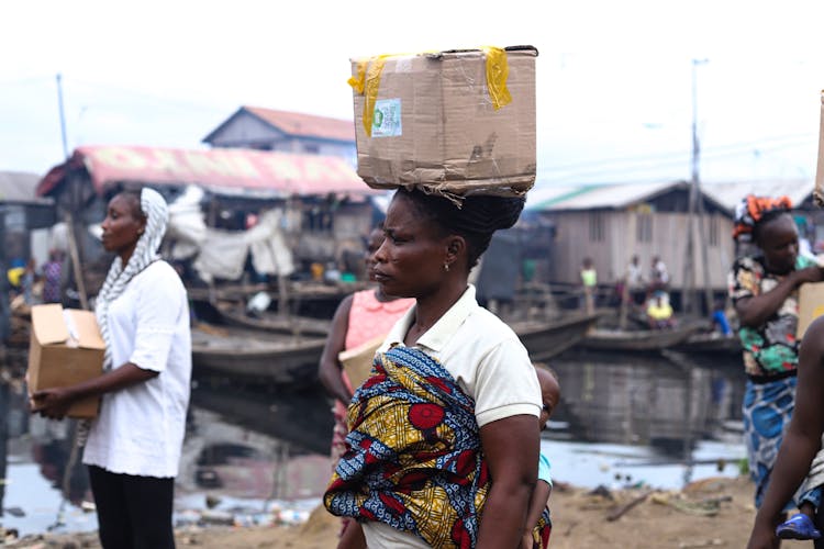 Side View Of A Woman Carrying A Cardboard Box On Her Head