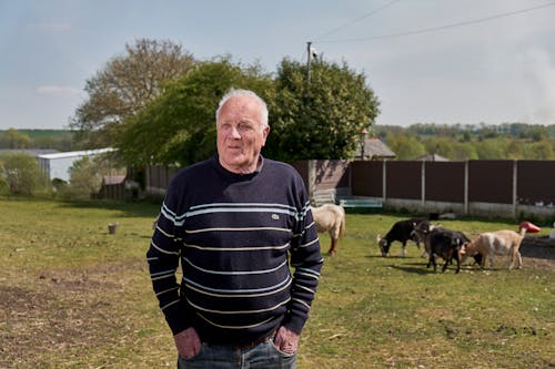 Man in Striped Long Sleeve Shirt Standing on Green Grass Field 