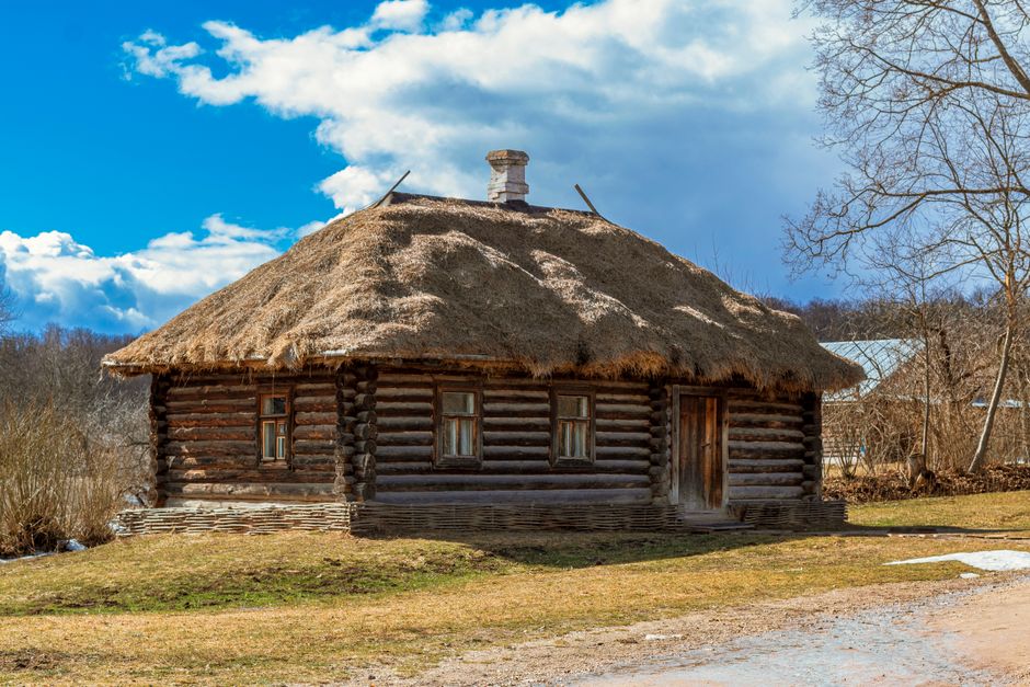 Charming wooden cabin with a thatched roof in the scenic countryside under a blue sky.